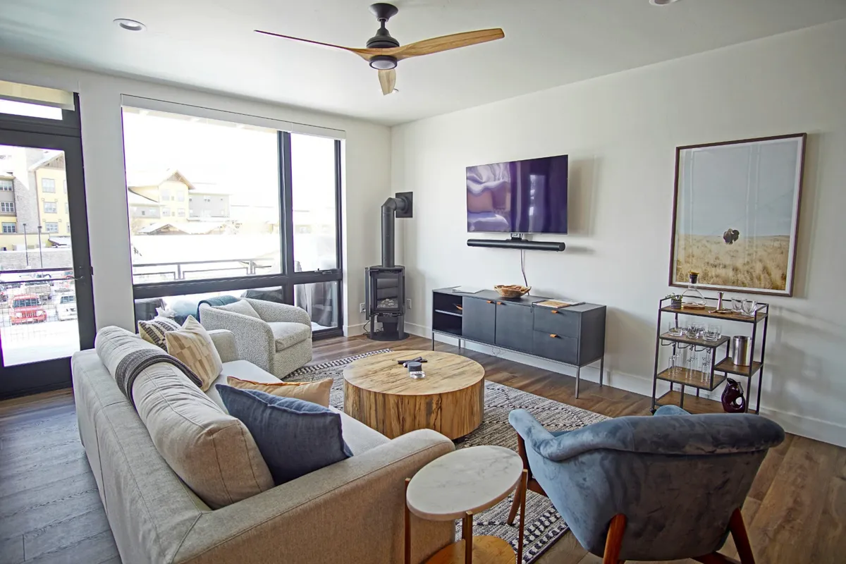 This image shows a modern living area featuring a comfortable sofa, coffee table, television, and large windows with scenic views and a fireplace. Natural light pours into the room, creating a bright and inviting retreat ideal for relaxing after outdoor activities or enjoying cozy evenings in all seasons.