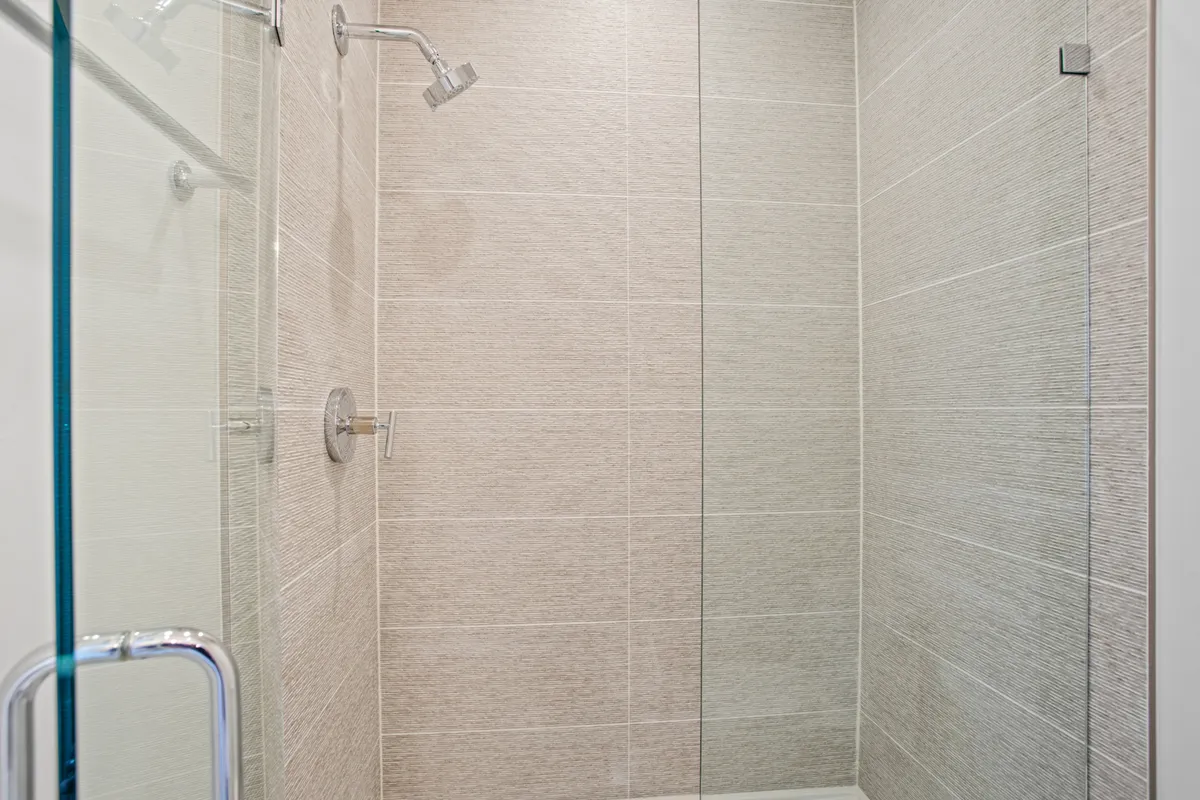 A modern bathroom featuring a sleek glass shower enclosure, premium showerhead, and textured wall tiles. The space invokes a refreshing and serene atmosphere, perfect for unwinding after a busy day of exploring or socializing.