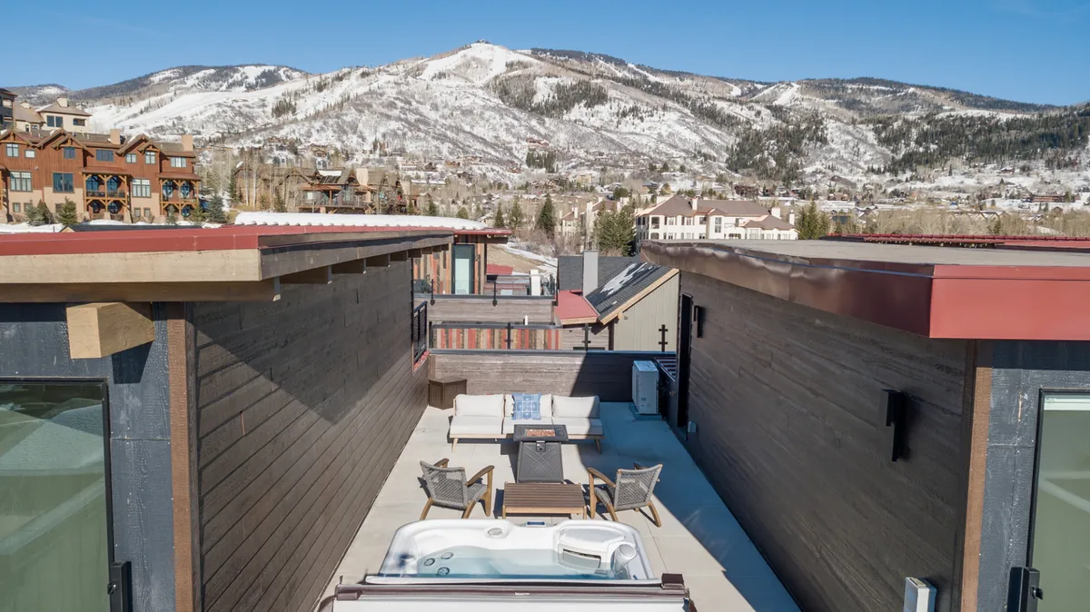 This image showcases a private rooftop hot tub surrounded by comfortable outdoor seating, all set against a breathtaking mountain backdrop. The area features inviting lounge furniture and is perfectly positioned for panoramic views of Mt. Werner and Emerald Mountain, with the hot tub as the central focal point. The scene is tranquil, ideal for relaxing, socializing, or enjoying stargazing sessions.