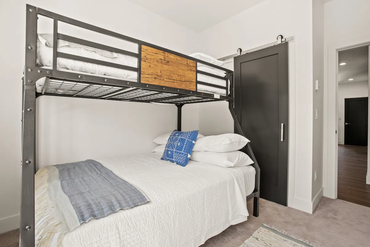 A cozy bunk room featuring a twin-over-full bunk bed dressed in white bedding, accented with a vibrant blue pillow. The space exudes a fun, family-friendly vibe—perfect for kids or groups—offering a playful yet restful sleeping area.