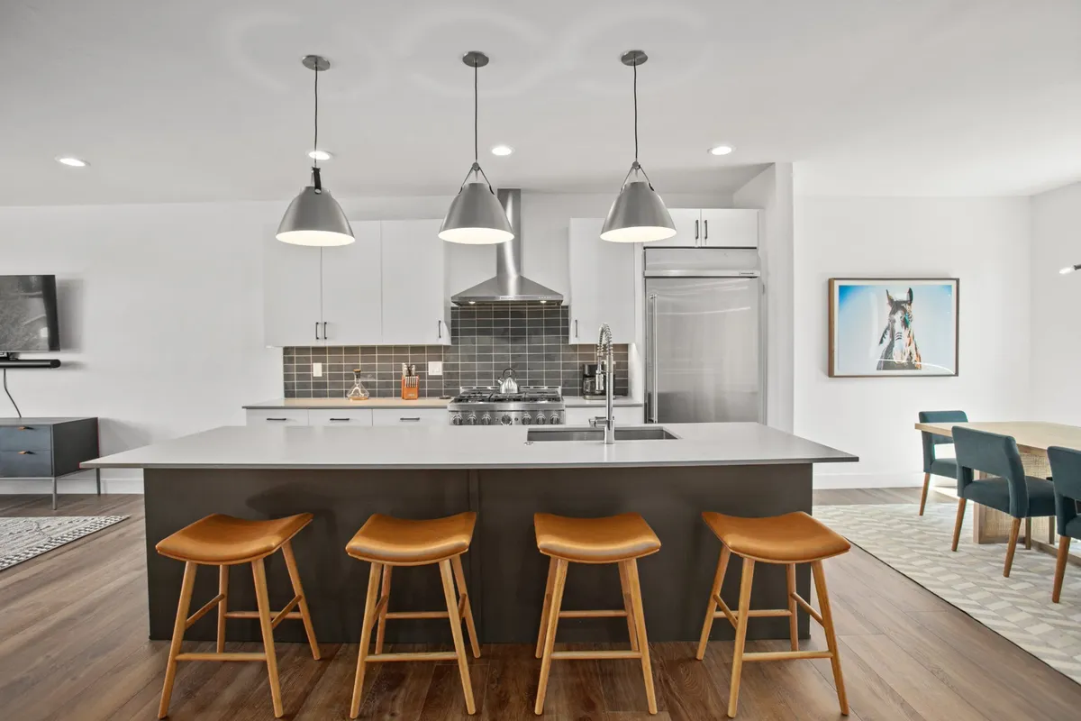 A stylish kitchen island with modern pendant lights and stools sits at the heart of a contemporary open-plan living space. Sleek appliances and subtle artwork add a sense of sophistication, while the island invites group cooking and casual dining.