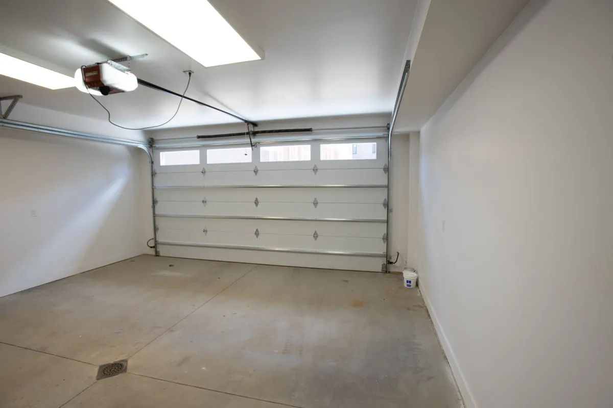 A bright, clean garage space with the garage door closed, modern ceiling lights illuminating the area, and a spotless floor. The environment is uncluttered, suggesting ample room for parking vehicles, storing sports gear, or setting up a personal workshop.