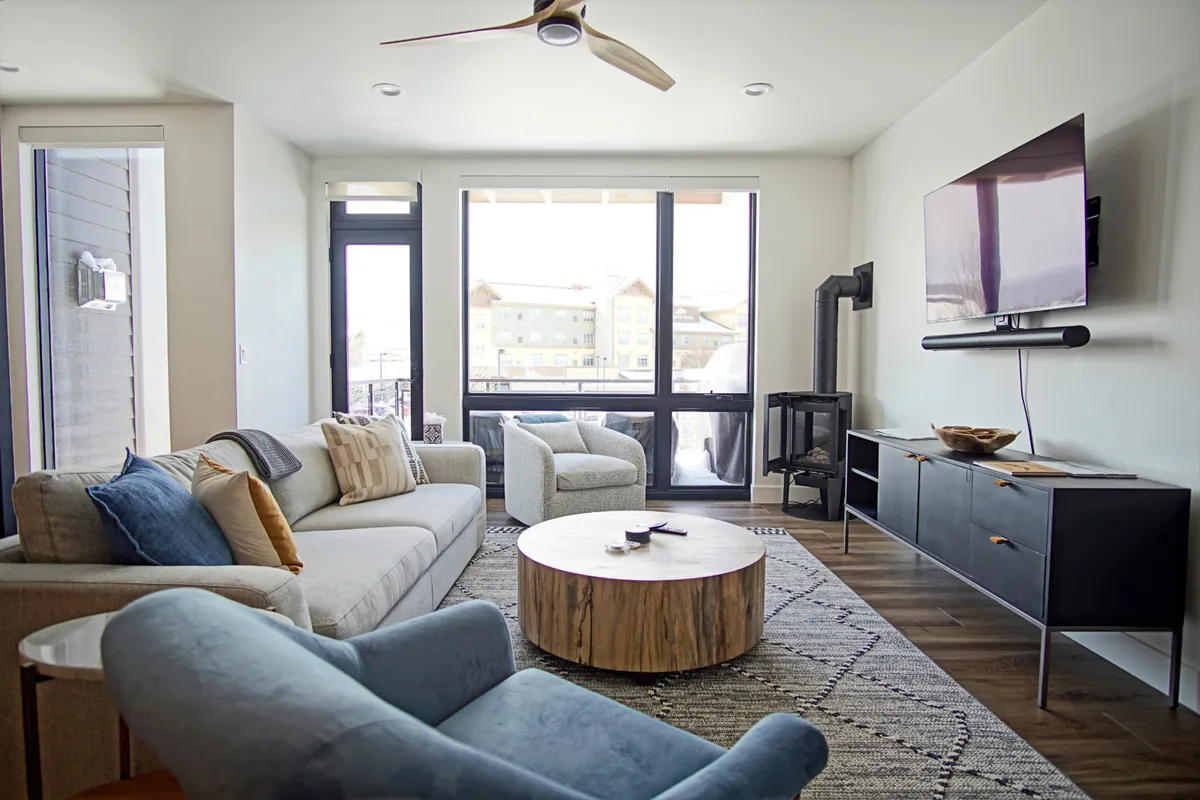 A modern living room with a cozy sofa, coffee table, and a large TV dominates the space. Natural light streams through the windows, creating a warm, inviting atmosphere for relaxing or socializing after a day of adventure.