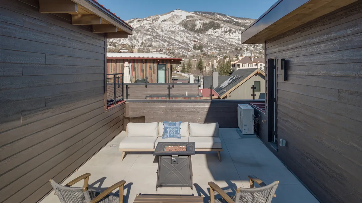 The photo presents an inviting outdoor seating area centered around a cozy fire pit table, with plush chairs and a breathtaking mountain view in the background. The setup is ideal for gathering with friends or family after a day outdoors, enjoying stargazing, or simply relaxing in comfort regardless of the season.