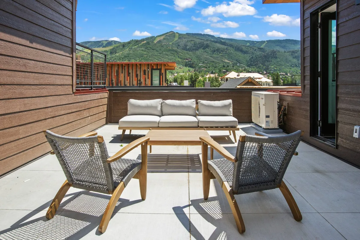 An inviting rooftop or terrace area featuring a sofa and chairs set against a dramatic mountain backdrop. The setting suggests a comfortable gathering spot for socializing, relaxing, or enjoying the panoramic view after a day outdoors.