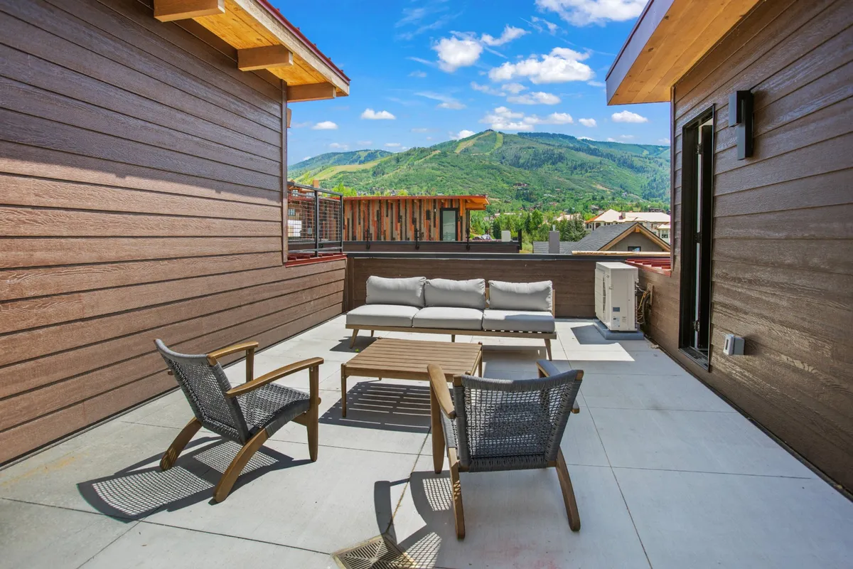 The exterior image showcases a stylish rooftop patio complete with comfortable outdoor seating, set against a stunning backdrop of the Rocky Mountains. The scene captures a tranquil, inviting atmosphere ideal for gatherings at sunset or unwinding beneath the stars, emphasizing the property's elevated vantage point and its seamless blend of urban luxury with natural beauty.
