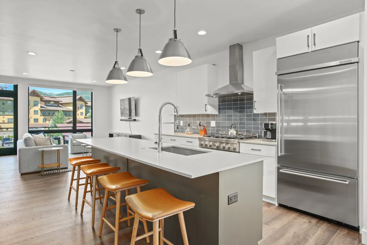 A bright, modern kitchen with a large island, bar stools, high-end appliances, and expansive windows. The setting is tailored for cooking, entertaining, and socializing, embodying the gourmet experience described.